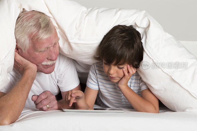 爷爷和孙子躺在床上用平板电脑