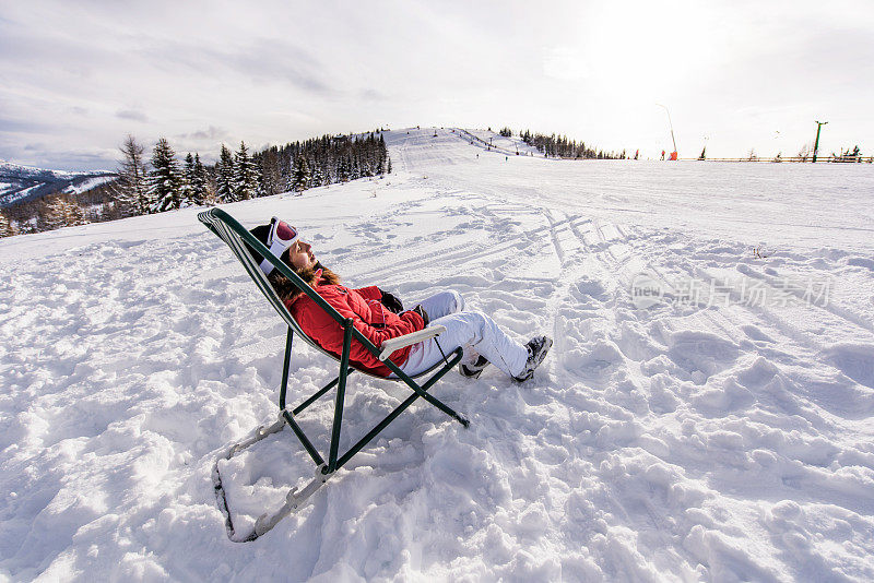 穿着滑雪服的女人在雪地上的躺椅上晒太阳。