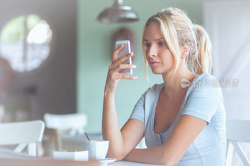一个沉思的年轻女子在咖啡馆里用智能手机输入短信