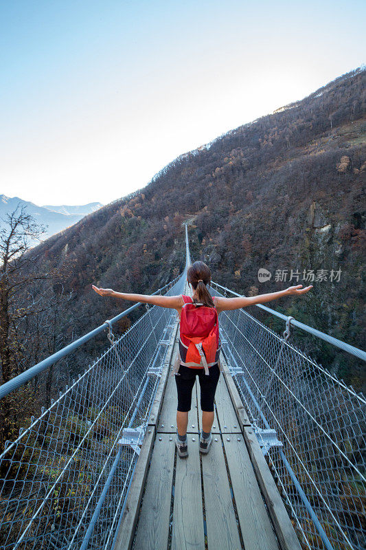 年轻女子在吊桥上徒步旅行，双臂张开