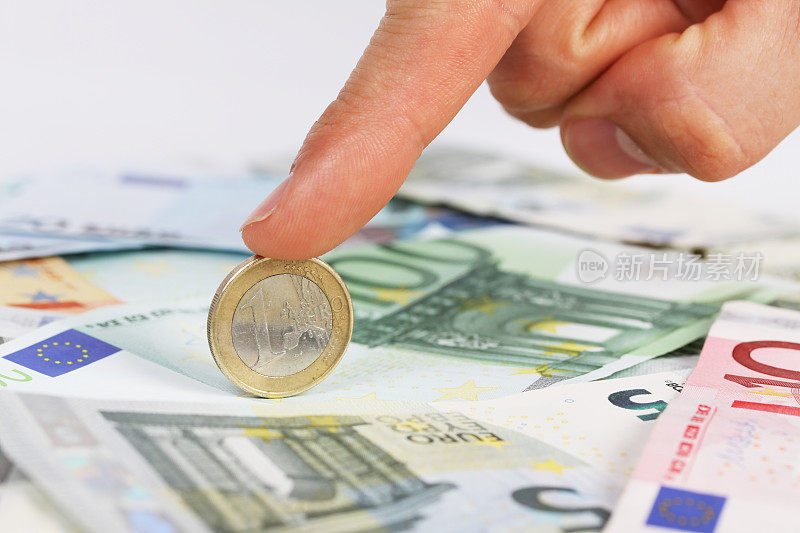 一个男人的手指拿着一枚欧元硬币在欧元纸币上