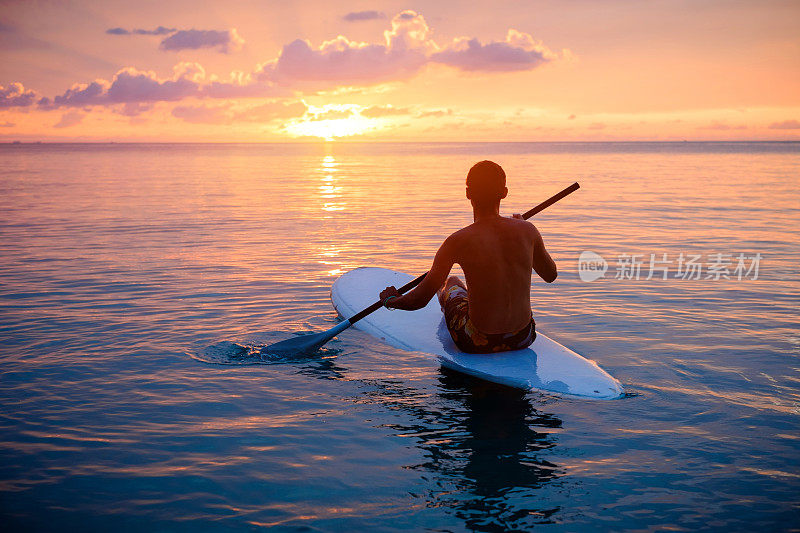 夕阳西下，男子在冲浪板上的剪影