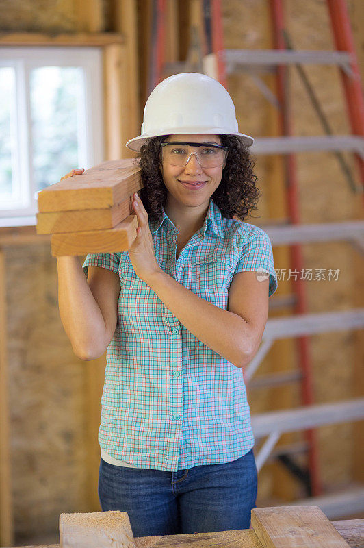 一名女建筑工人扛着一堆2x6的木材，准备进行室内改造