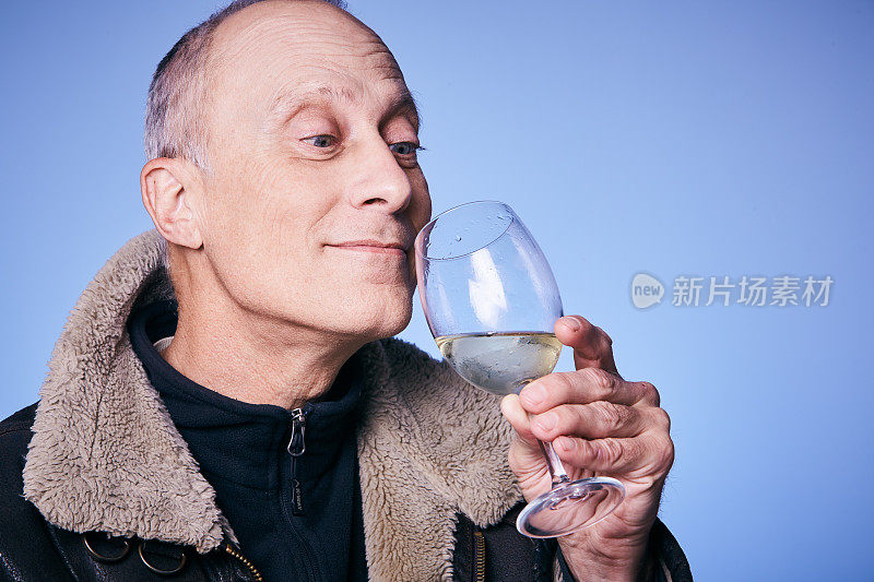 一个成熟的男人举起酒杯，欣赏地闻着白葡萄酒