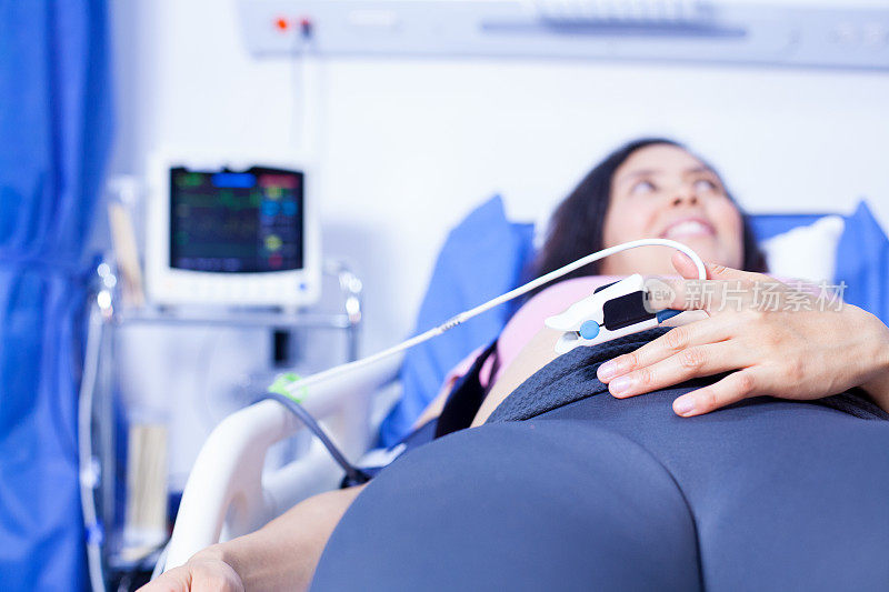 拉丁裔孕妇，躺在担架上手指上戴着心率监测器