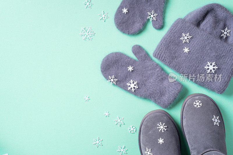 冬天暖和的衣服平躺着。羊毛女装毛衣，围巾，靴子，蓝色背景的雪花。俯视图，复制空间