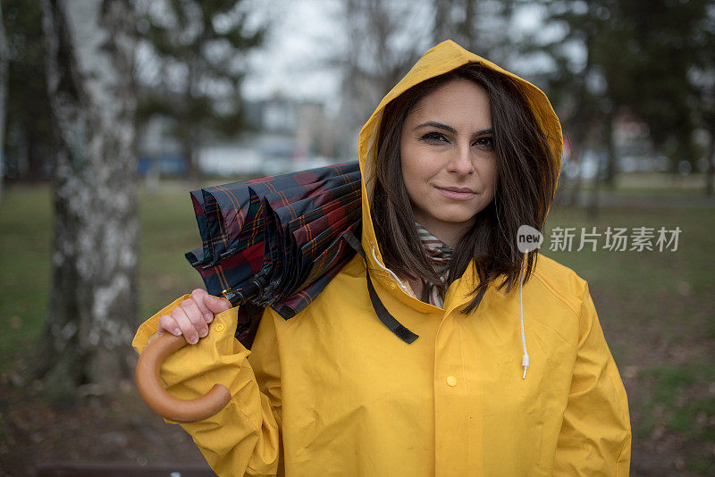 穿着黄色雨衣的年轻女子在公园里度过雨天