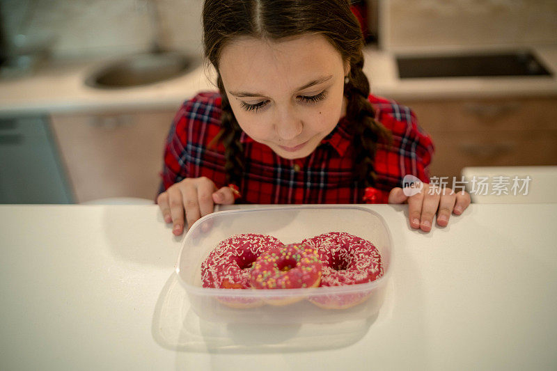 对孩子的饮食。悲伤和不快乐的孩子触及甜甜圈。孩子们的美味食物。孩子在看甜甜圈。垃圾食品上瘾。