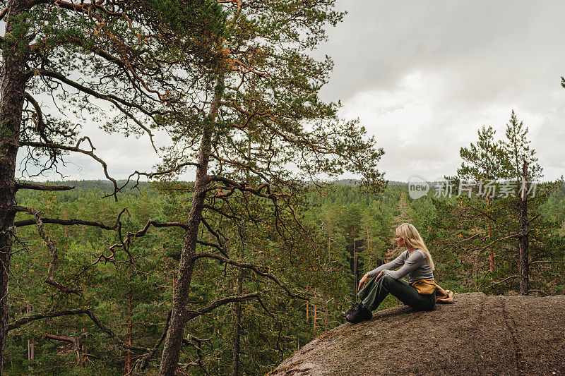 女人坐在悬崖上远足在野外森林自然景观的小径