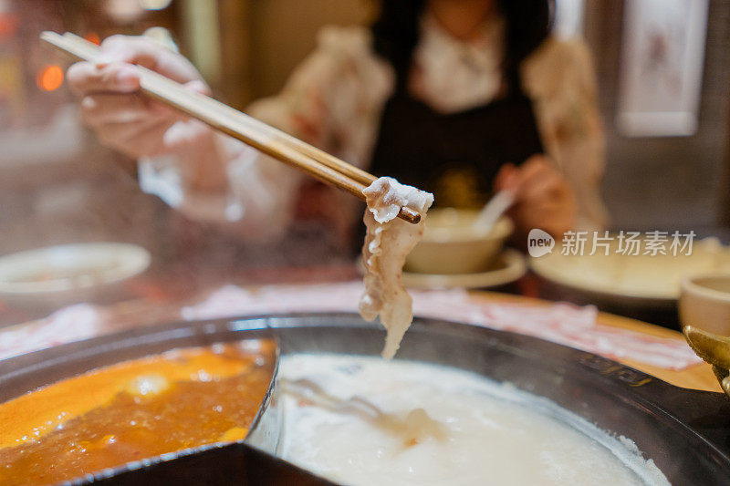 一位亚洲的中国妇女用火锅汤煮猪肉片
