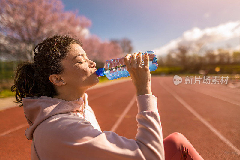 运动的年轻女子在运动轨道上跑步后喝水。