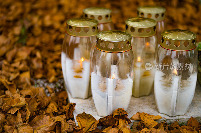 白色的灯笼挂在坟墓上，周围是褐色的秋叶。