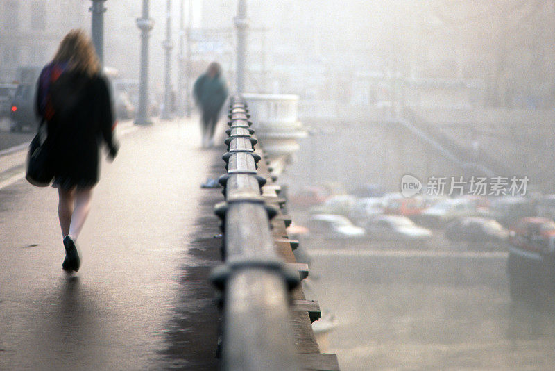 从后面的女人走在城市的一座桥上，在雨天