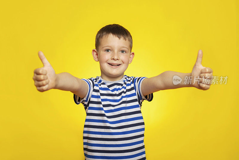 快乐男孩的肖像在条纹t恤显示拇指向上的手势在黄色的背景。