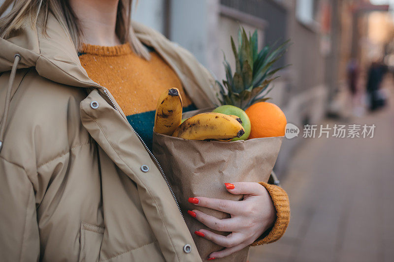 一个年轻的女人拿着一个装着新鲜水果的纸袋