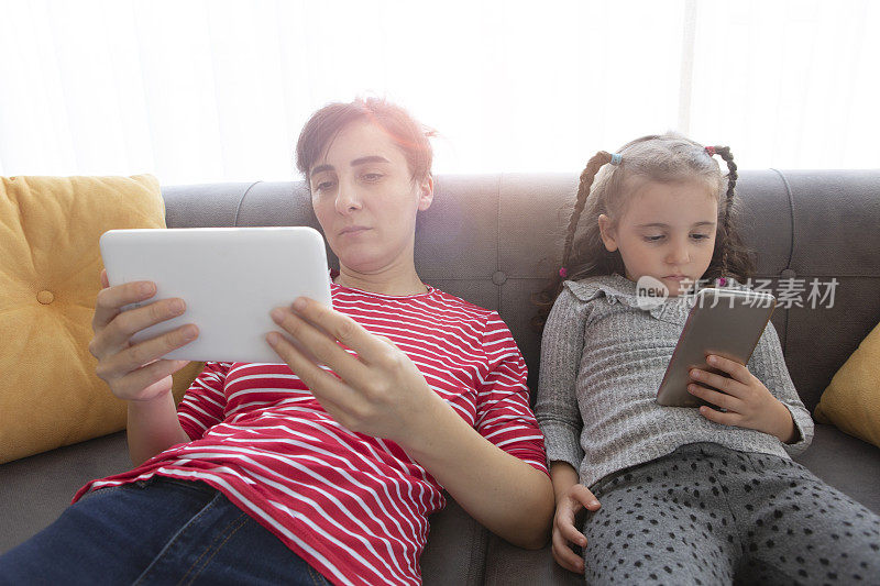 妈妈和小女儿一起使用平板电脑和智能手机放松
