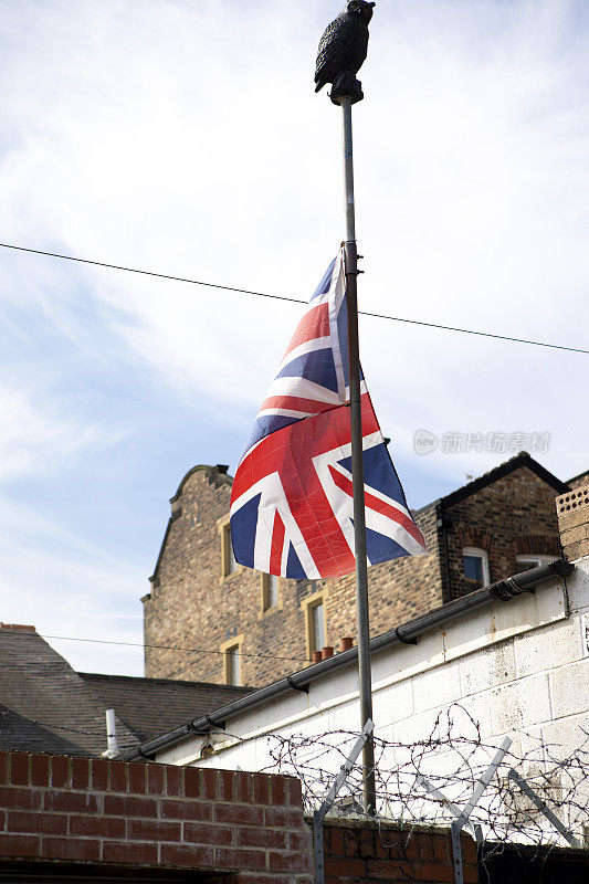 市中心房屋的后院，墙上挂着带刺铁丝网，英国国旗在那里降半旗