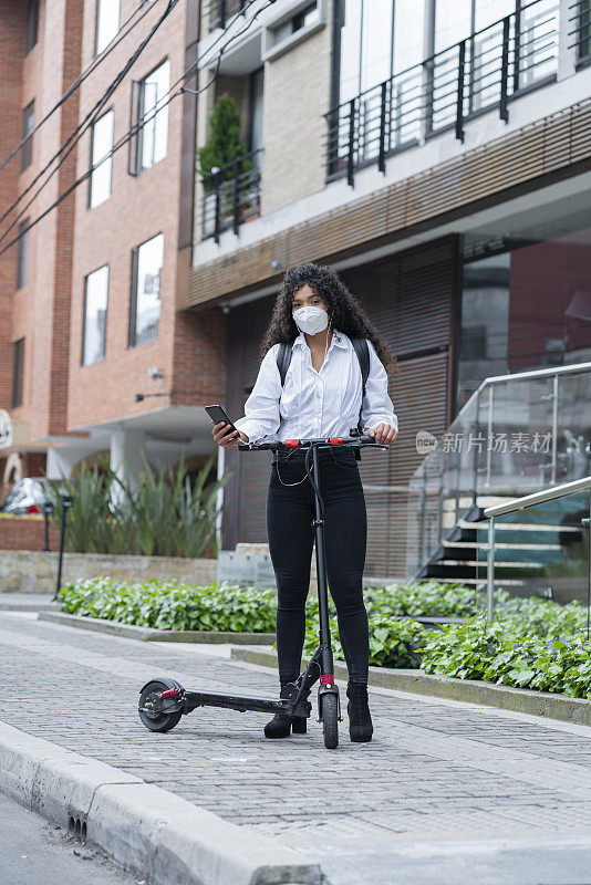 一个年轻的卷发黑发女人骑着她的电动滑板在街上听着音乐去工作的肖像