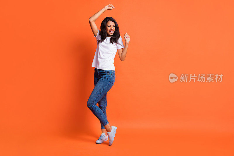 全长照片的女孩跳舞看空的空间穿白色t恤牛仔裤鞋孤立的橙色背景