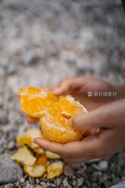 年轻女子在岩石海滩上吃橘子当早餐