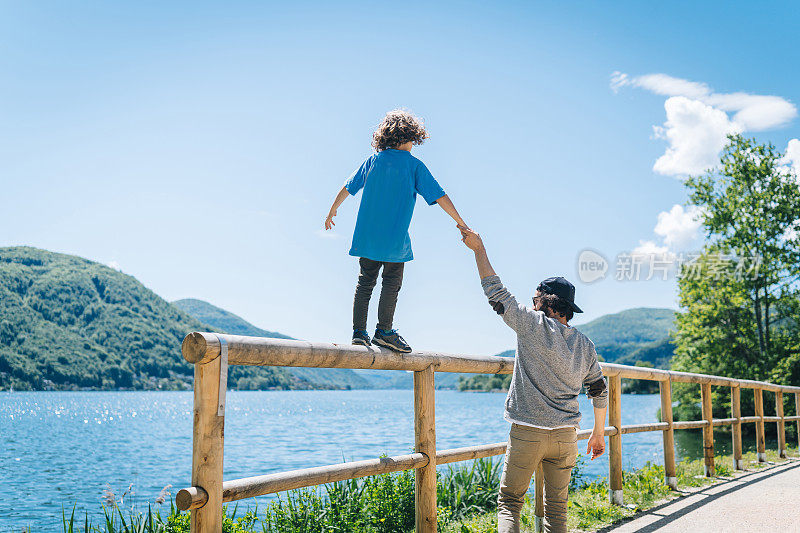 小男孩沿着卢加诺湖附近的木栅栏走着，保持着平衡