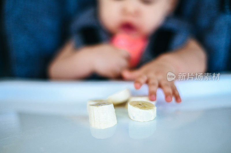 宝宝正在尝试一种新的食物，他伸手去拿香蕉片