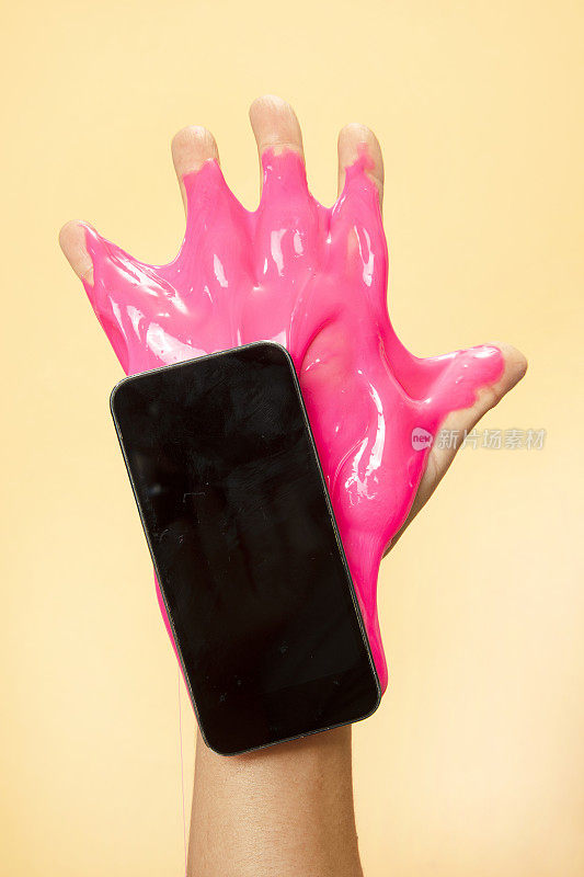女人的手使用智能手机与霓虹灯粉色黏液玩具在橙色流行艺术背景。