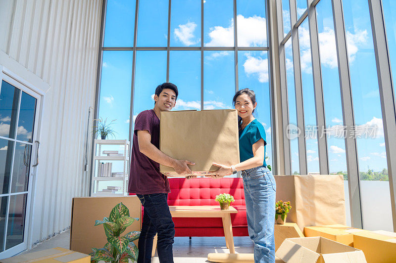 搬家日，年轻的亚洲夫妇带着大纸板箱喜笑颜开，庆祝搬新家的概念