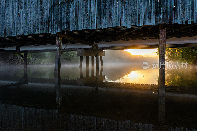 日出背后的风雨覆盖的桥上平静的雾蒙蒙的河水