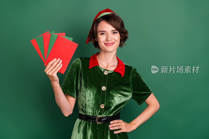 漂亮的邮差助手女士拿着扇子信封，戴着精灵服装帽子孤立的绿色背景照片