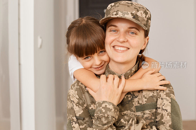 从部队回来或锻炼后，带着露齿微笑的女孩和她的女儿合影，孩子拥抱她的妈妈，想念她的女儿。