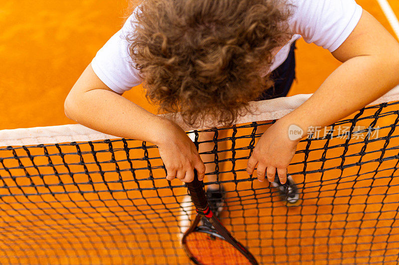 网球运动员，在比赛间隙靠在网球网上放松