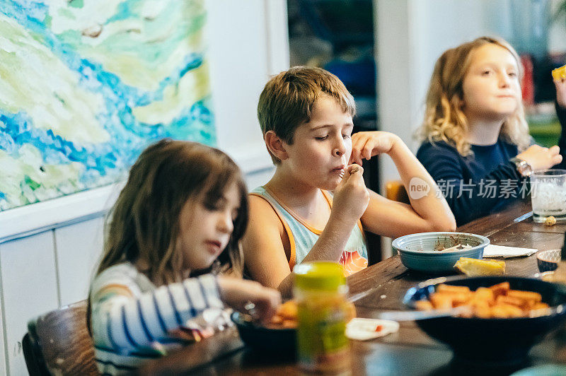 三个兄弟姐妹在家里的饭桌上一起吃饭，一家人