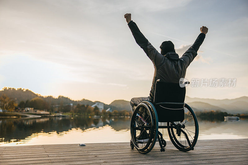 残疾人坐在轮椅上，在码头上举起双臂