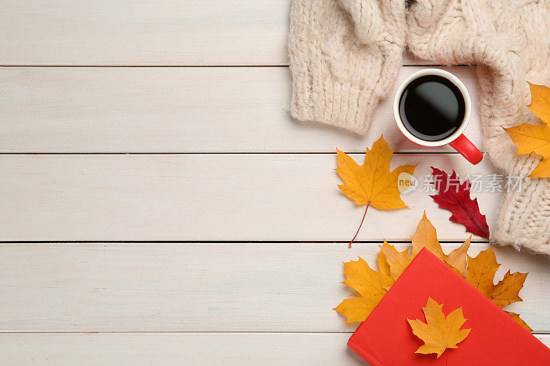 一杯热咖啡，书，毛衣和秋叶放在白色木桌上，平躺着。空间的文本
