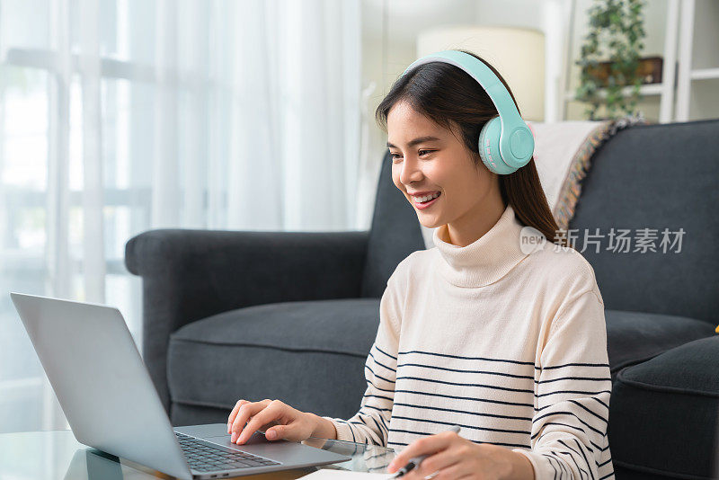 开朗美丽的亚洲女人戴着耳机，使用笔记本电脑在视频电话会议和网上学习。
