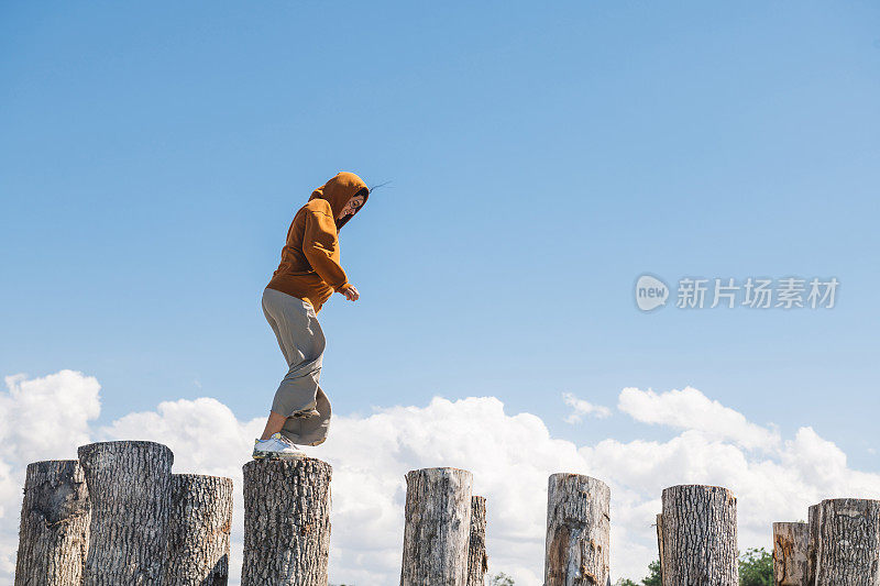 穿橙色连帽衫的少女在高高的木桩上保持平衡