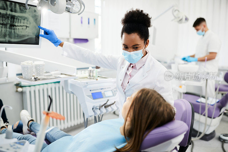 黑人女牙医在牙科诊所向青少年病人解释牙科x光。
