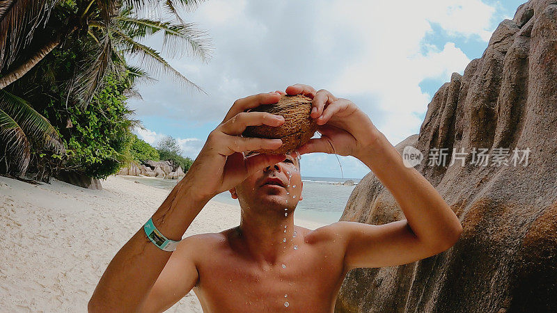 一名年轻人在海滩上喝椰子汁。