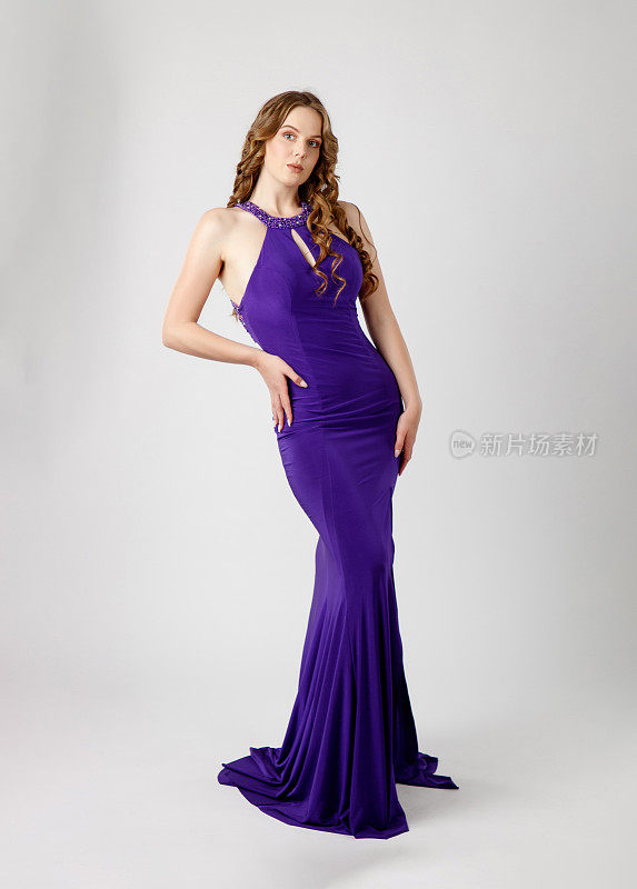 美丽的时装模特穿着紫色的无袖连衣裙，手放在臀部看着镜头