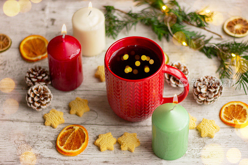 桌上放着红杯的圣诞茶，上面有针织图案，旁边放着饼干、香料和蜡烛