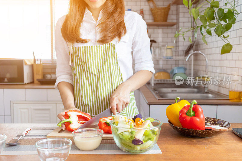 一名年轻女子正在为她的早餐准备甜椒，并准备在餐桌上享用健康的有机蔬菜。健康食物准备方法