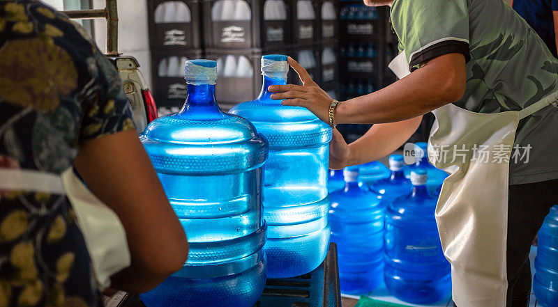 工人们把几加仑的蓝色饮用水和装在板条箱里的瓶子搬到一辆运输卡车的后面。