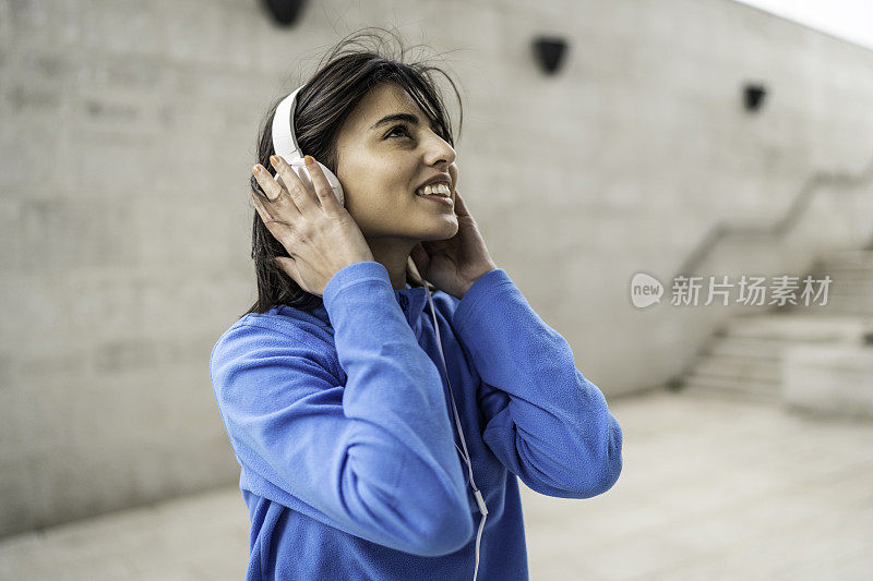 年轻快乐的运动女子在城市背景听音乐