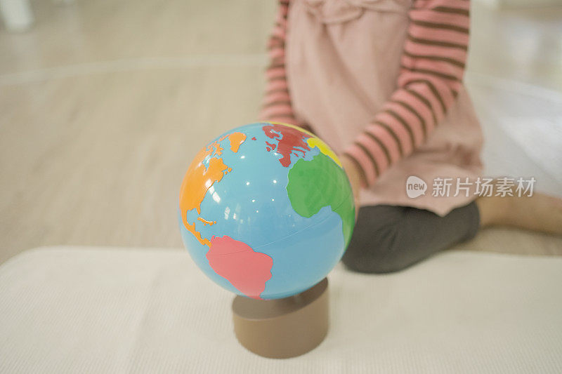 学龄前女童在蒙台梭利教育学校和家庭教育中使用模型地球仪学习世界地图