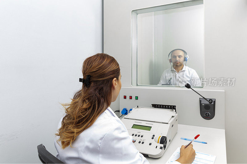 女听力学家在私人录音室用听力计对男病人进行听力检查。