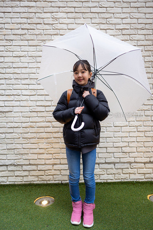 下雨天，日本一名小学生背着“随机书包”站在白色的墙上