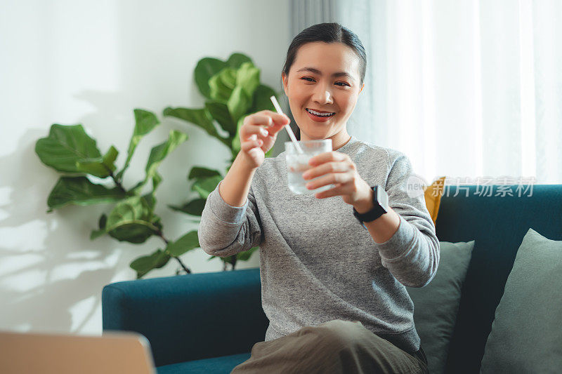 亚洲妇女坐在客厅的沙发上，用稻草搅拌水和冰休息。