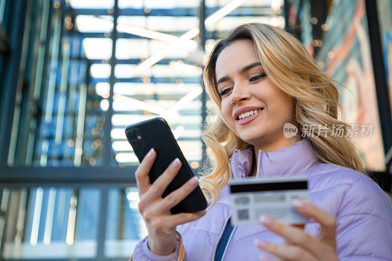 移动购物便利:金发女子用信用卡对着手机微笑
