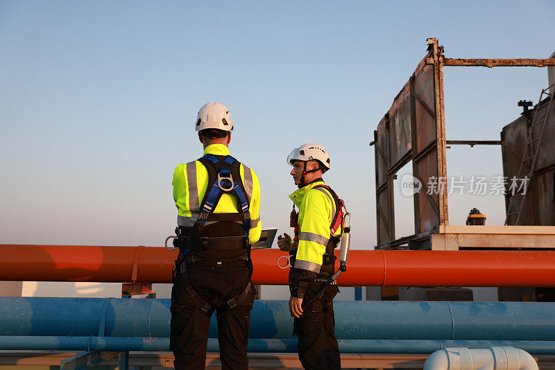 在工业环境中，两名男技术人员穿着安全束带修理暖通空调冷却系统的冷水机。